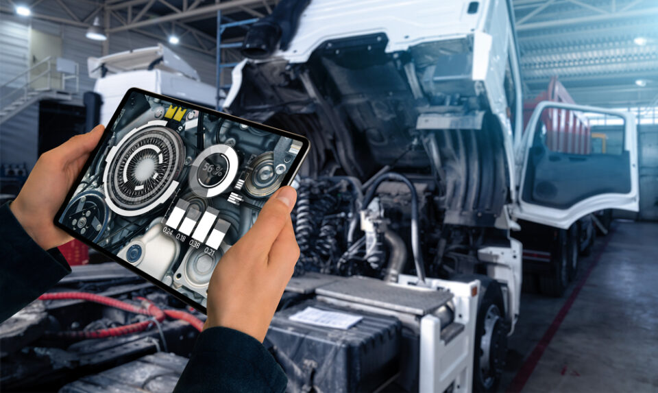 Mechanic's hands holding a tablet in front of a semi-truck with the hood up.